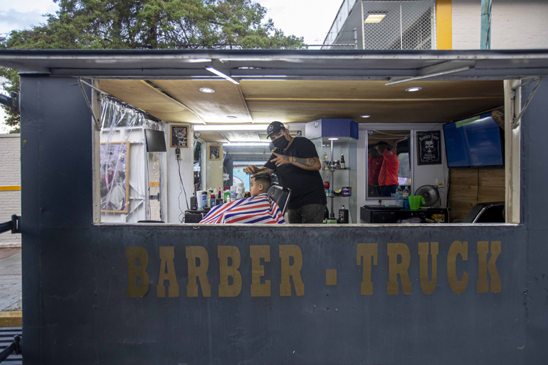Mexican barber Gerardo (R) gives a haircut to a customer